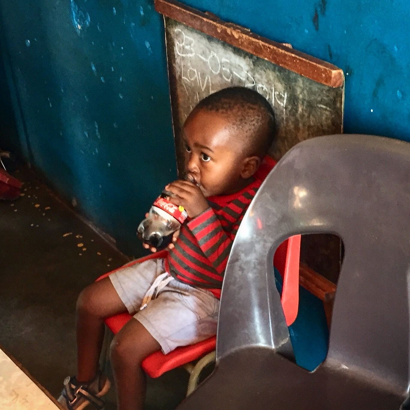 Child sitting on a chair drinking from a bottle in a room with blue walls.