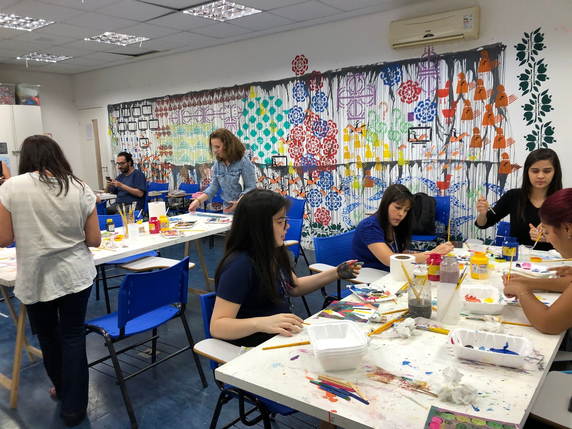 People participating in a colorful art workshop, working on various painting projects with supplies spread across tables.